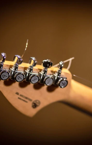 A wooden guitar headstock with chrome tuning pegs and loose strings, set against a blurred background. A wooden guitar headstock with chrome tuning pegs and loose strings, set against a blurred background.